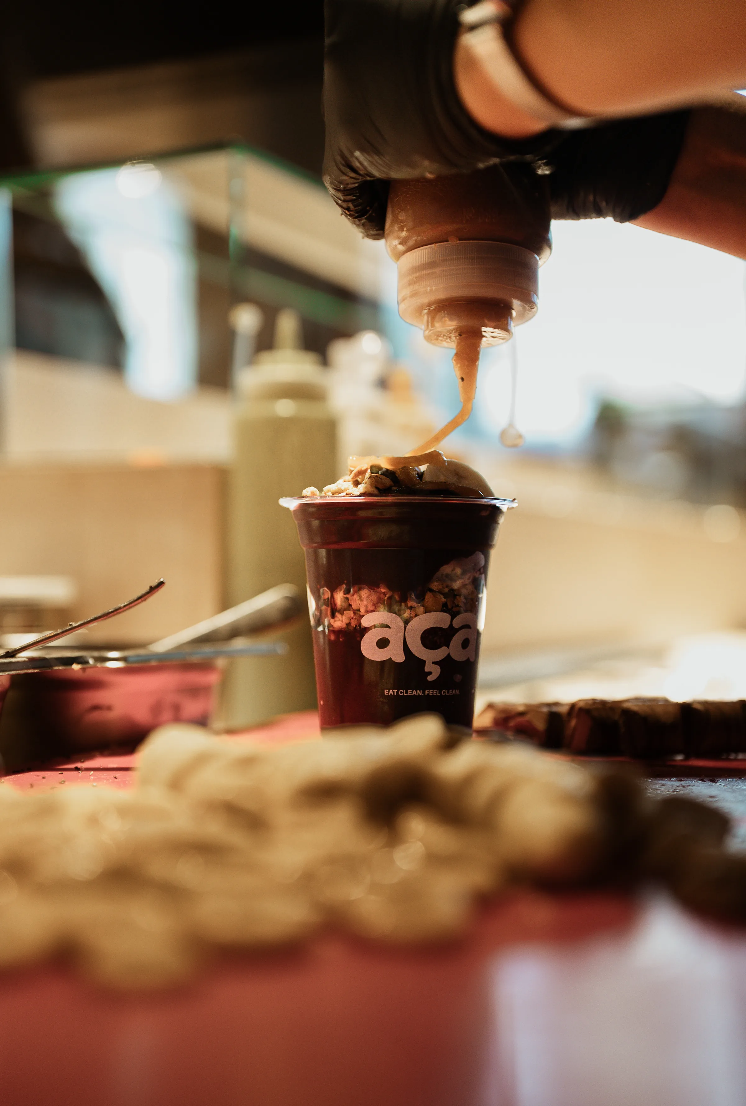 Eine Açaí Bowl im aça Becher wird am Tresen mit Sauce übergossen